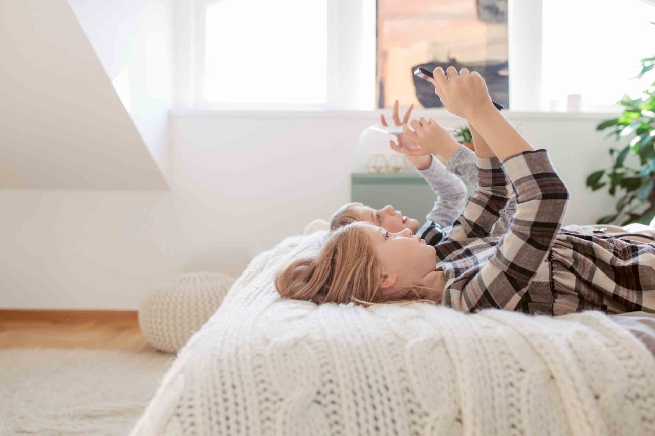 Boy and girl lying on bed and looking at tablets.