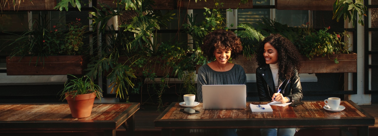 Two women sitting with a laptop and notepads at a coffee table. Business colleagues working while having coffee at a coffee shop.