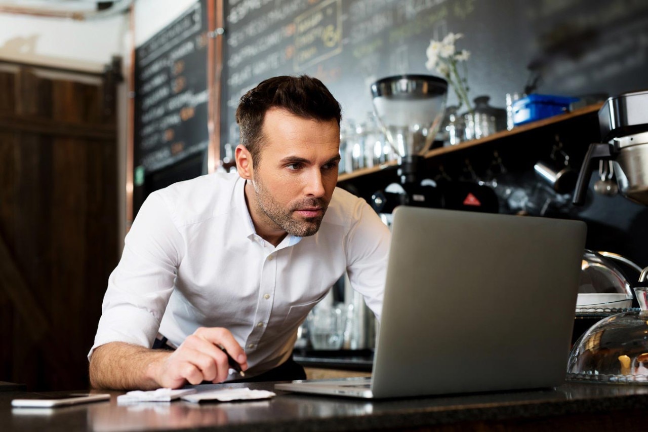 Restaurant manager working on laptop, counting small business income