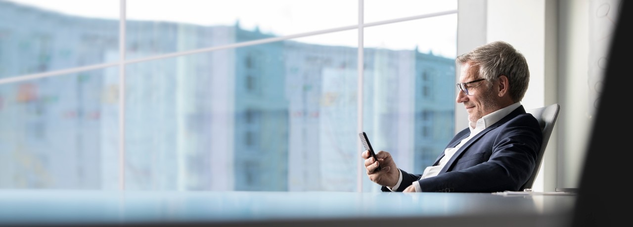 An elderly man in office attire studying information on his phone