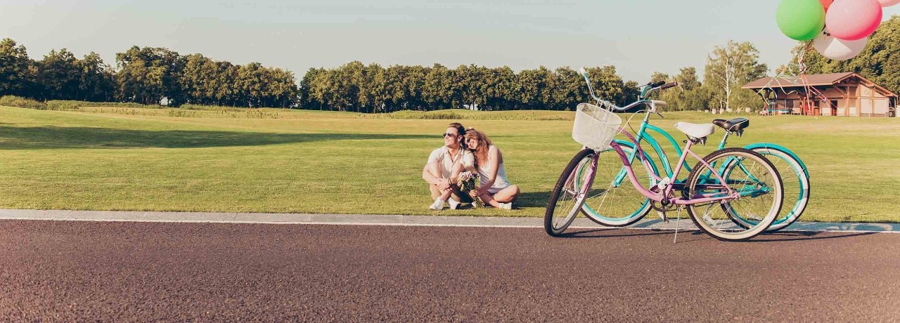 romantic happy couple in love sitting on the grass at their bicycles