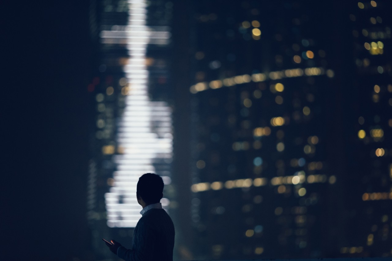 Busy businessman text messaging on smartphone while looking over city skyline and highrise commercial buildings at late night.