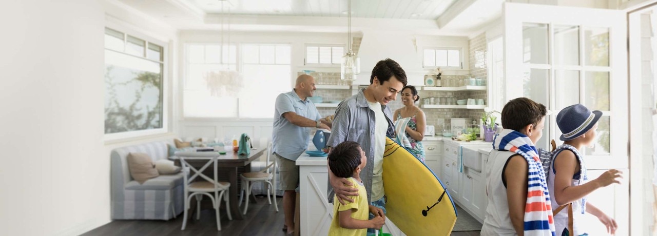 A family with beach attire and surf boards exiting a house smiling.