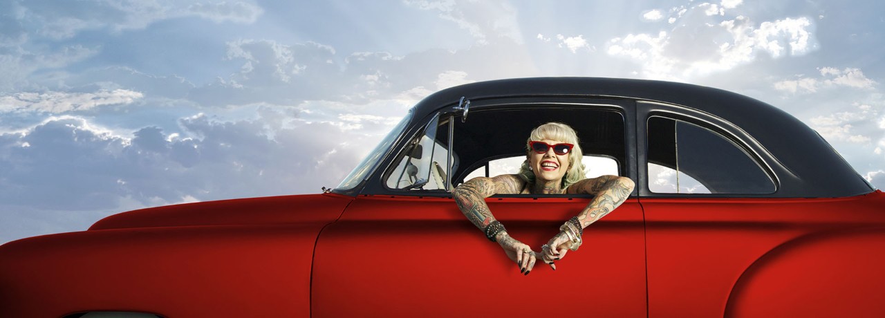 A woman in a red car, smiling and looking out the window