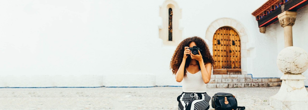 A woman sitting outside takes a photo  while travelling.